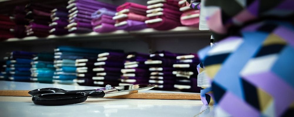 Regal mit gefalteten Stoffen, davor eine Schere auf dem Zuschnitttisch